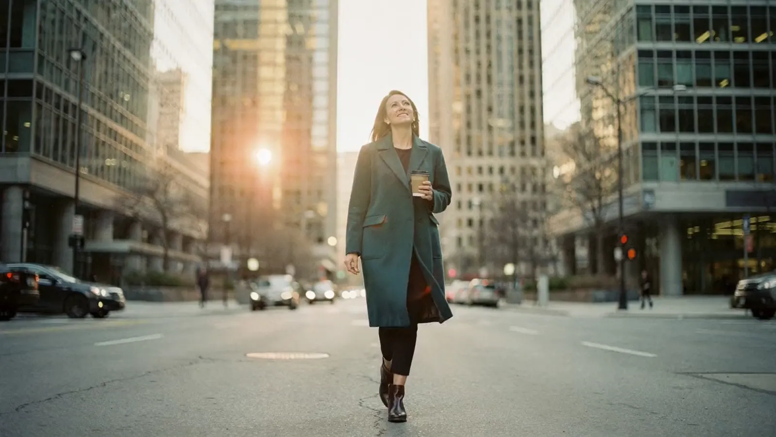 A woman in a teal coat walks through downtown Toronto at golden hour: down the street, past the office towers, across a plaza